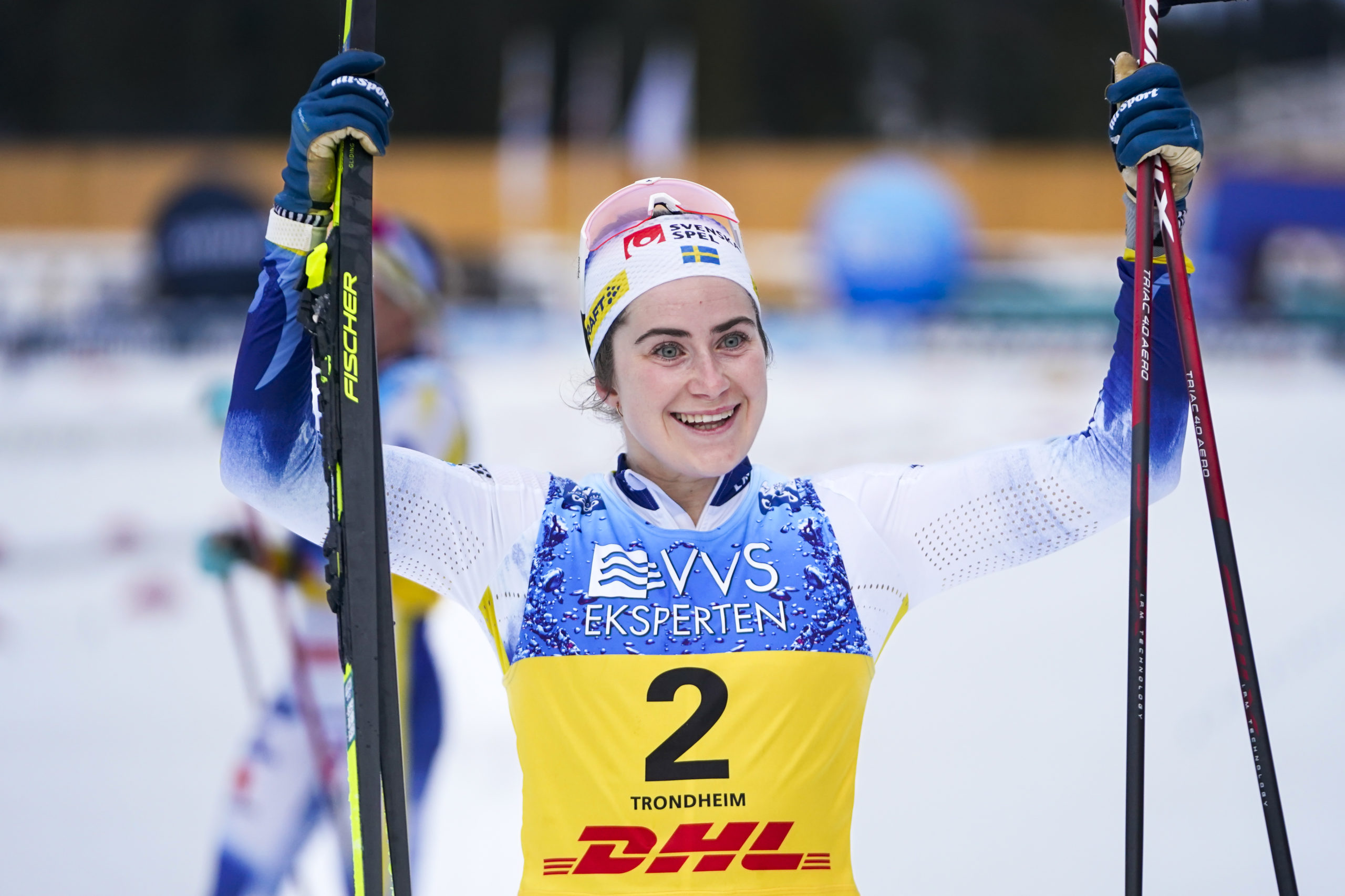 Ebba Andersson ler och håller upp stavar och skidor i luften efter vinst.